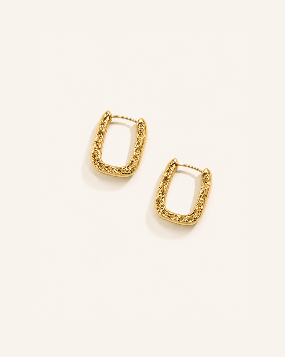 A pair of waterproof gold earrings on a plain background